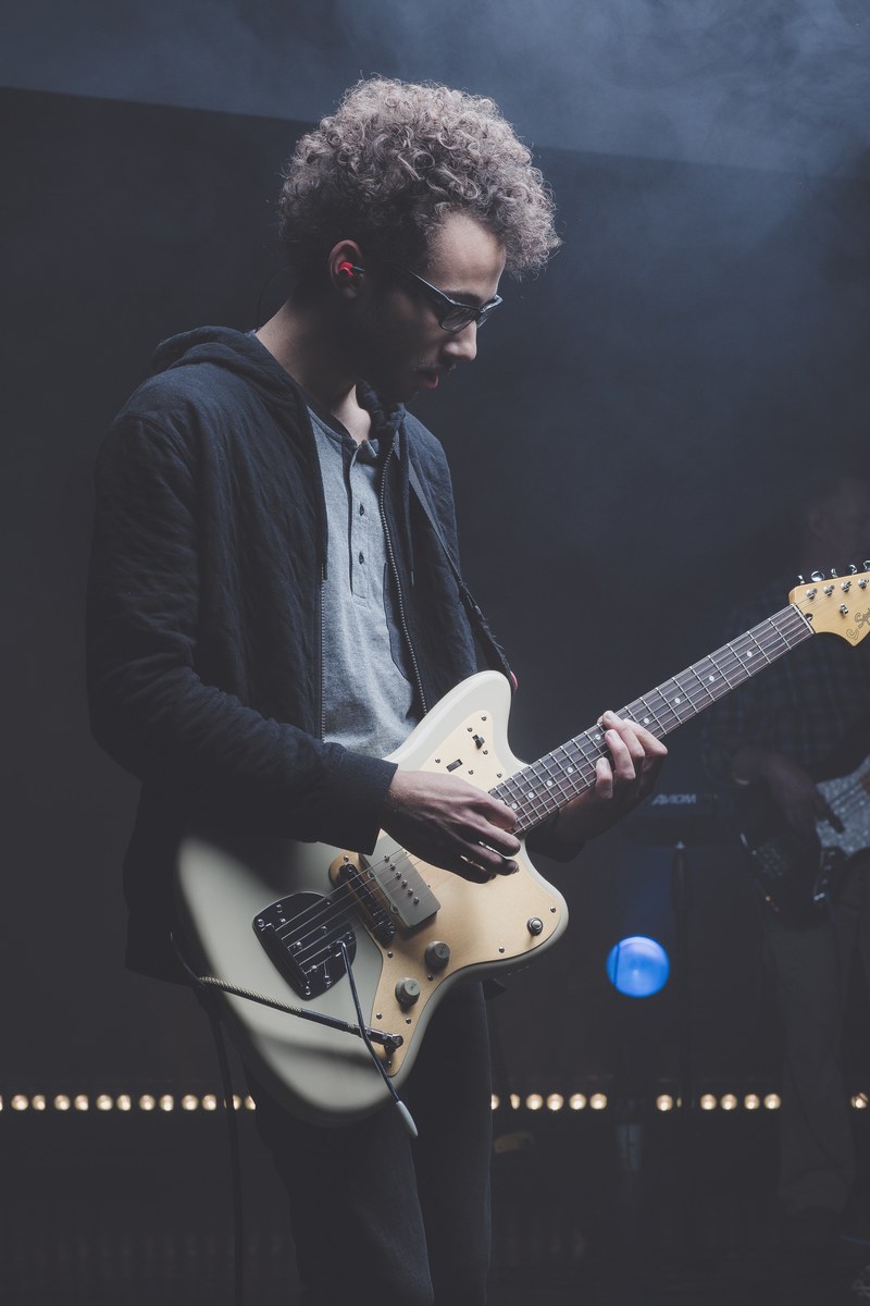 a young man in glasses playing electric guitar on stage in colorado springs, guitarist in glasses performing live 4k