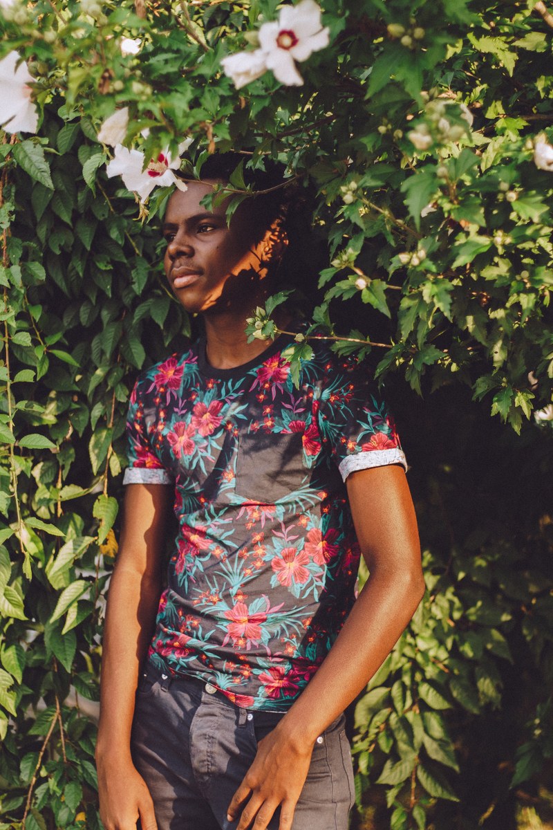 a person in a floral patterned shirt stands among green foliage looking to the side, person outside in floral shirt 4k