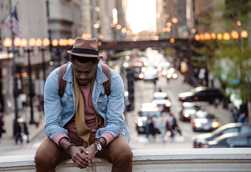 a man in a leather jacket looking down while sitting on a ledge in a city, there is always hope 4k