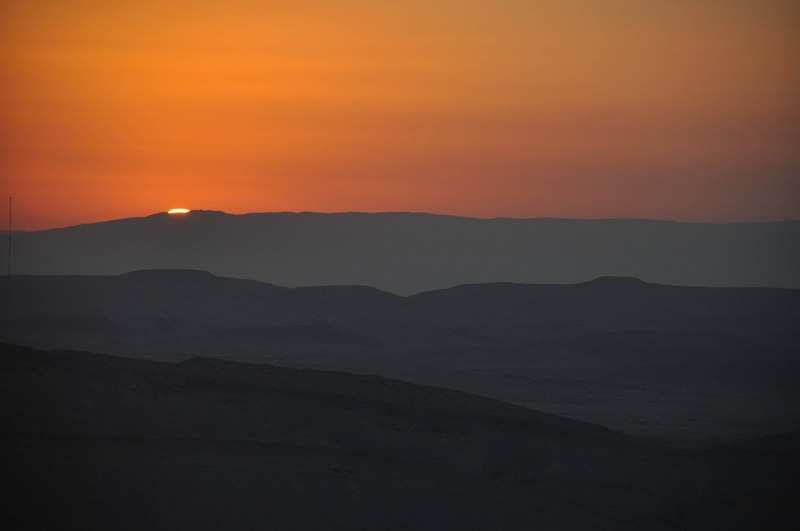 setting sun almost entirely obscured by the silhouette of a mountain range on the horizon, sunset behind the mountains 4k