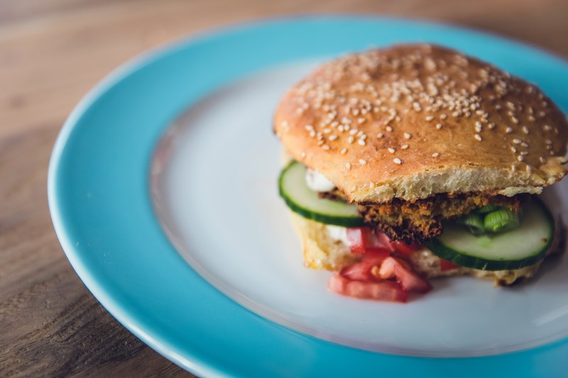 vegetarian burger on hamburger bun with cucumbers and tomatoes on blue and white plate, veggie burger on plate 4k
