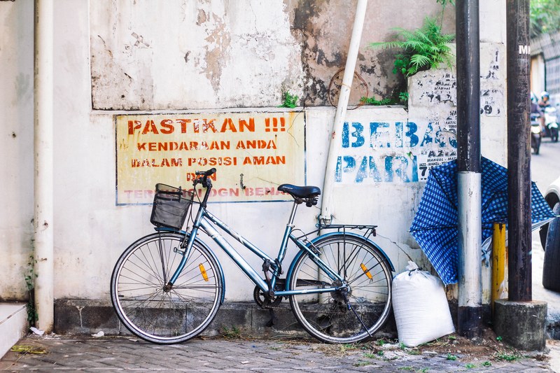 a bicycle with a basket leaning against a wall with graffiti and political messages on it in malang, bike to where 4k