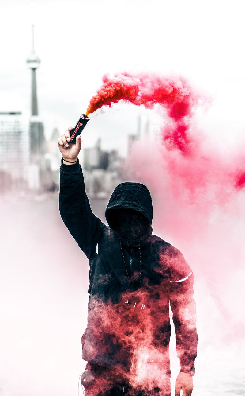 a person in a black hoodie with obscured face holds up a pink smoke grenade, person with pink smoke grenade 4k