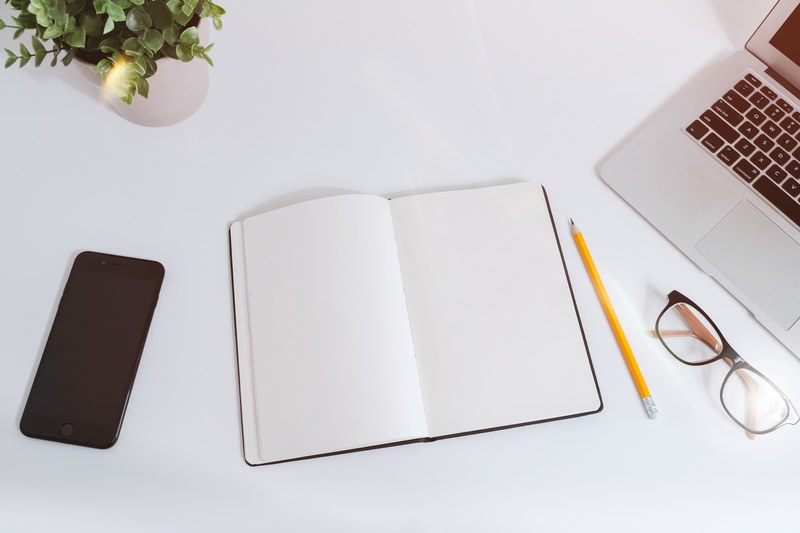 an open empty notebook on a white desk next to an iphone and a macbook, white work table with notes smartphone and laptop 4k