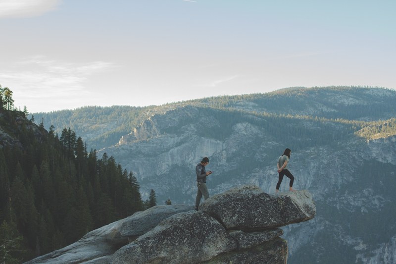 extreme hikers peer over a rock ledge atop a mountain landscape, extreme mountain views 4k