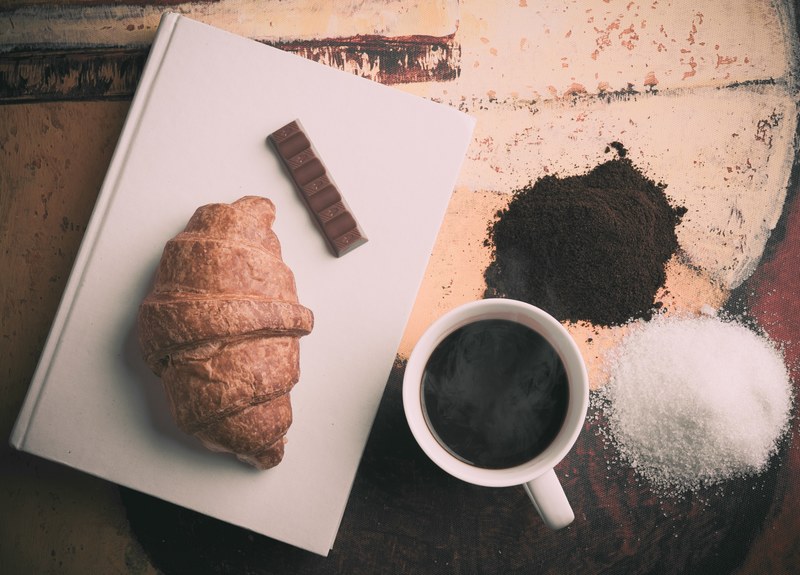 a croissant chocolate book coffee cup sugar and coffee grounds on a table, breakfast spread 4k