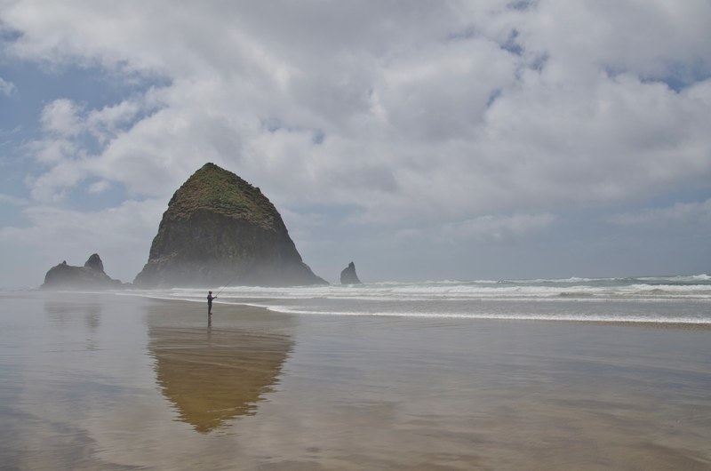 person fishing on the wet sand beach with the big rock formation in background at cannon beach, person fishing on cannon beach 4k