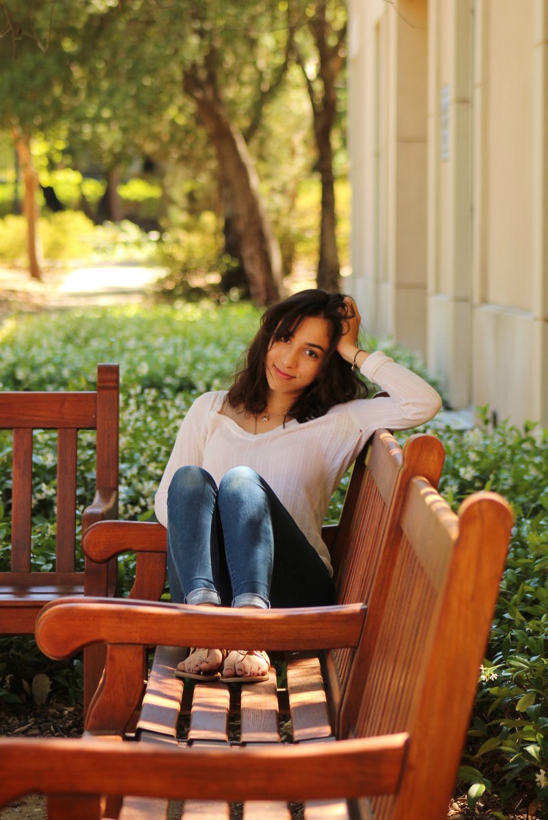 portrait of a woman smiling on a bench on the stanford campus with her knees up, woman on stanford bench 4k