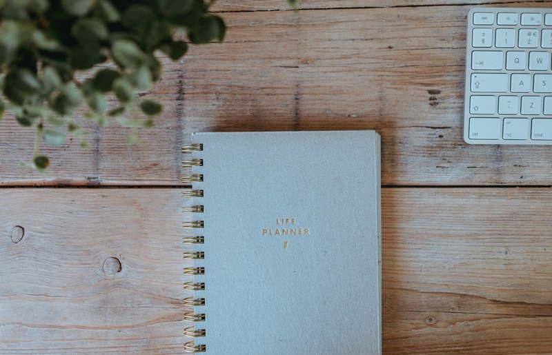 a life planner notebook on a wooden surface with a keyboard and a plant in the upper corners, life planner 4k