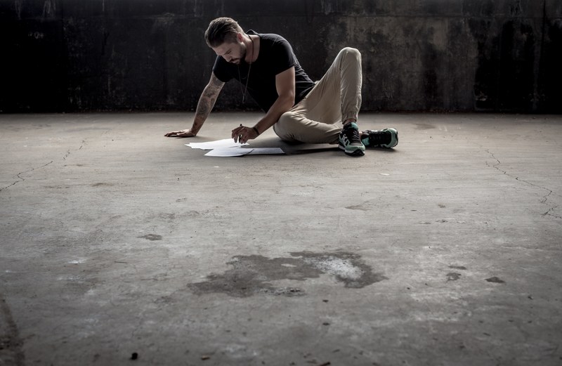 a man with a pen looking at sheets of paper while seated on a concrete industrial floor, man writing on concrete floor 4k