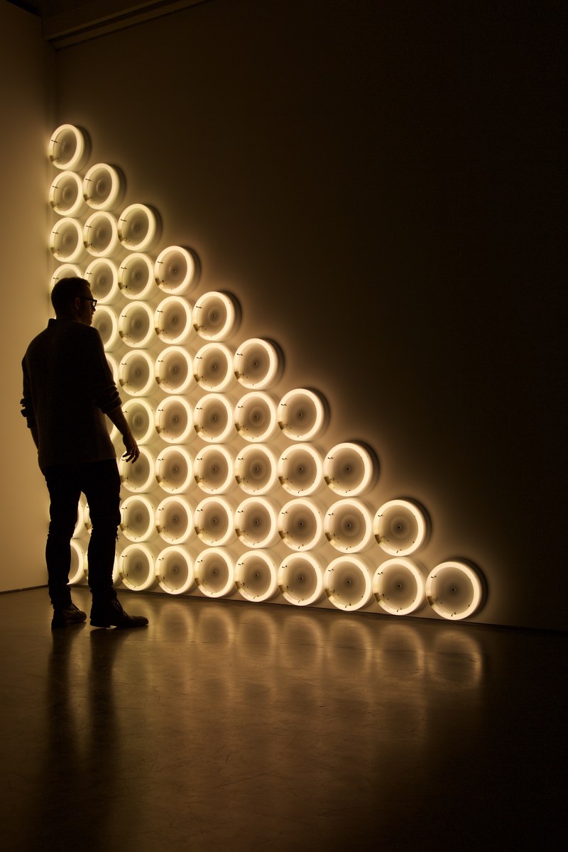 silhouette of man standing in front of triangular brightly illuminated lamp artwork in art gallery, silhouette lamp artwork 4k