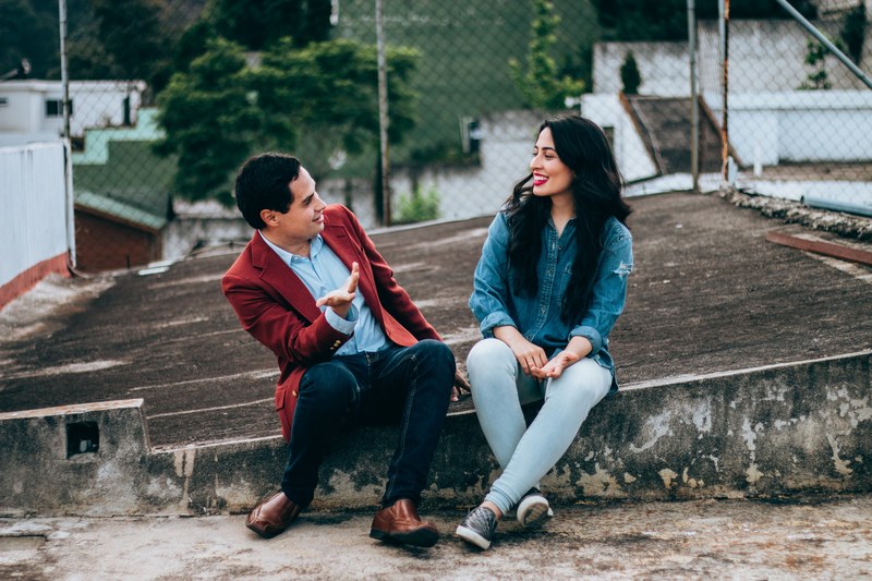man in ithaca sitting next to a woman on a rooftop making her laugh, friendship 4k