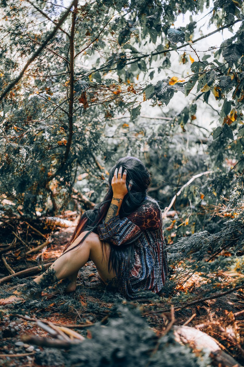 a woman with a forearm tattoo holding her hand over her face while sitting in the woods, _trapped 4k