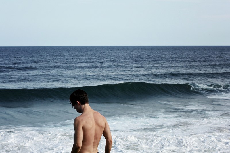 a shirtless man staring down as the waves come in at a beach in fingal head australia, thinking at sea 4k