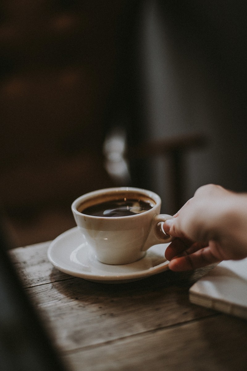 a person holding a cup of coffee in their hand in a cafe in george town, hot coffee on a rainy day 4k