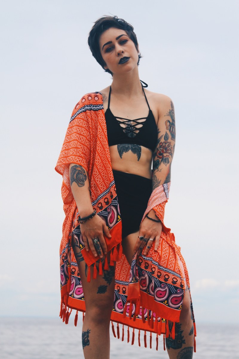a short haired woman in a black bikini wearing an orange cover up by the ocean, woman in bikini by the ocean 4k