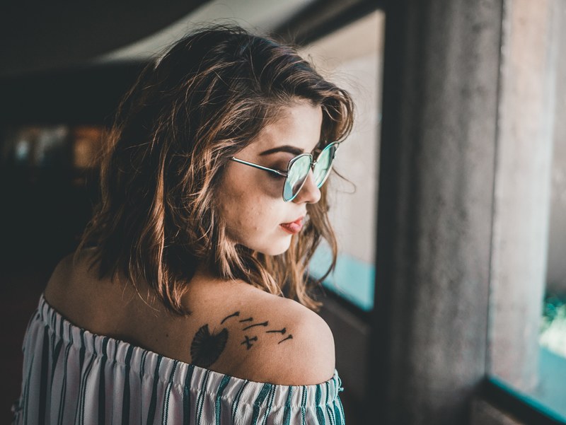 a woman in sunglasses wears an off the shoulder top which shows a tattoo on her back, _lookin over her shoulder 4k