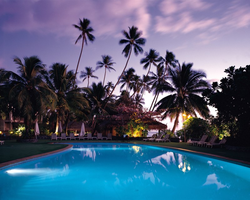 palm trees and deck chairs near a blue swimming pool at sunset, exotic swimming pool at sunset 4k