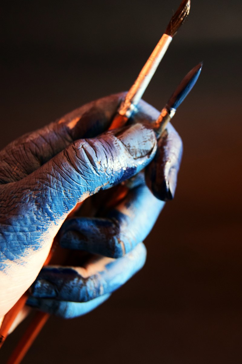 close up of a persons hand covered in blue paint holding two paintbrushes, blue magic 4k