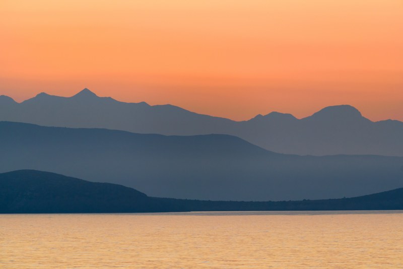 an orange sky at sunset over the tranquil water and peloponnese mountains, peloponnese sunset over mountains and water 4k