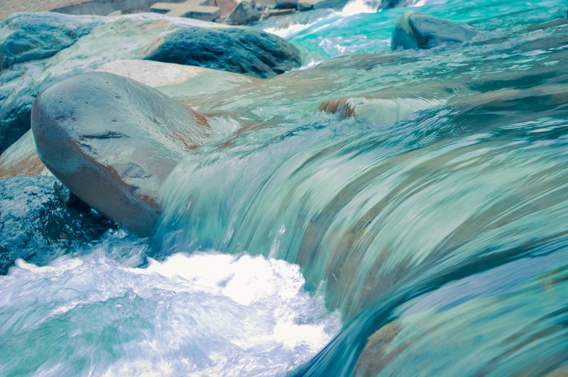 a close up of clear turquoise water flowing down the rocky river bed, smooth turquoise water 4k