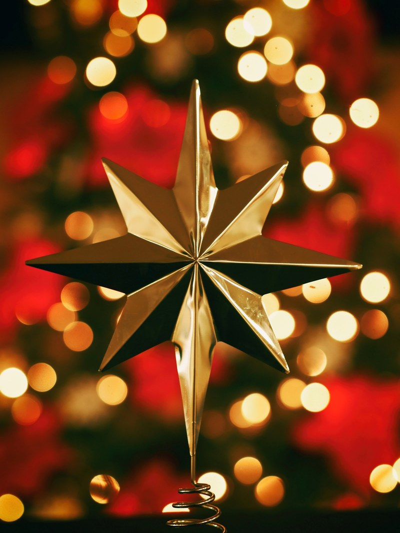 single gold star in center with unfocused christmas lights and flowers behind at christmastime, christmas star 4k