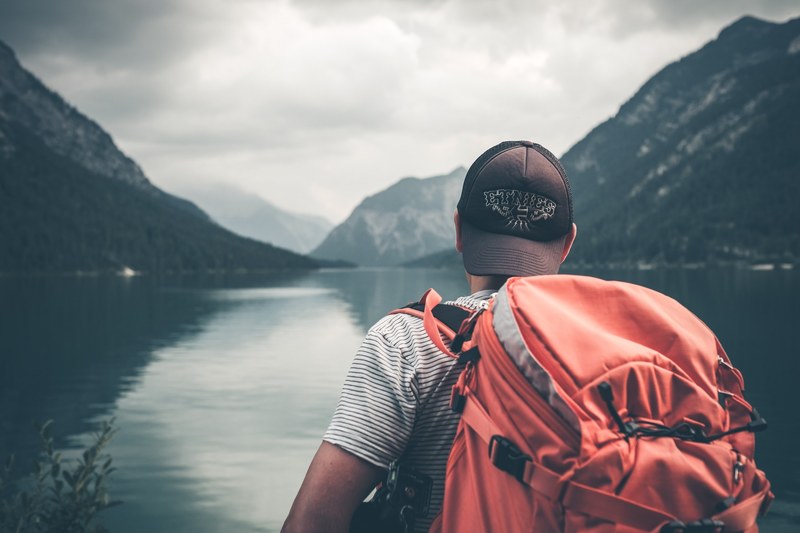 hiker with a heavy backpack looking out at mountains and still water, mountain backpacker 4k