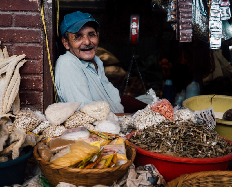 a smiling elderly man at his stall with dried seeds and spices, happy worker 4k