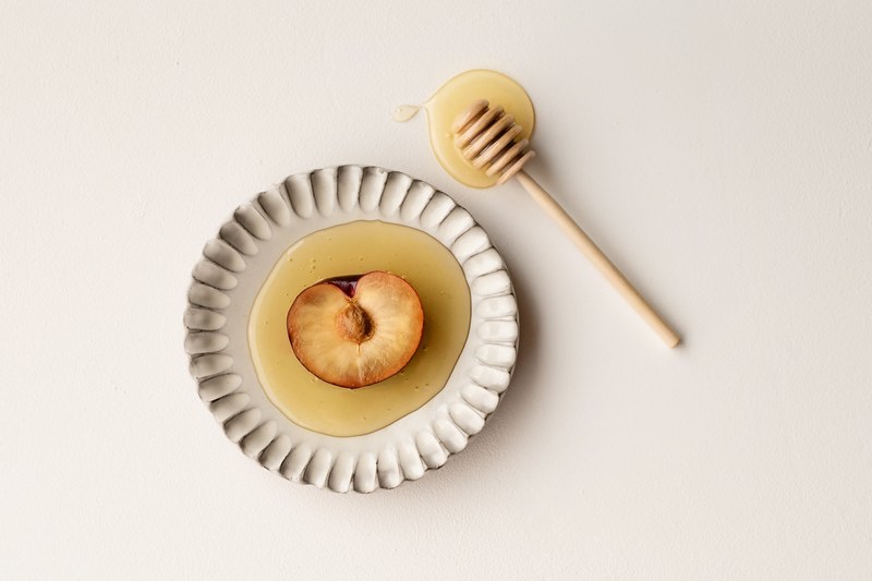 plum covered in honey on a white decorative plate with a honey stirrer nearby, sweet plum 4k