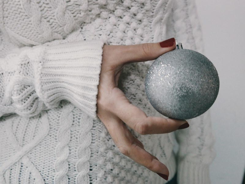 a person wearing a knitted sweater holding a silver christmas ornament, _holding xmas ornament 4k