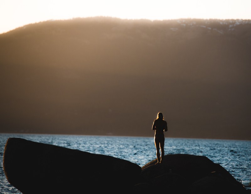 silhouette of a person standing alone on a rock near the water, sunset silhouette 4k