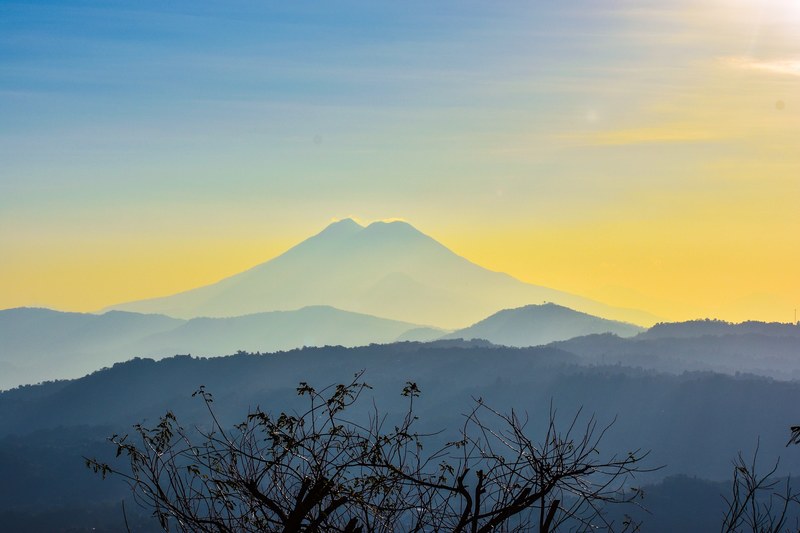 a pale silhouette of a tall mountain crest on the horizon during sunset, yellow dawn 4k