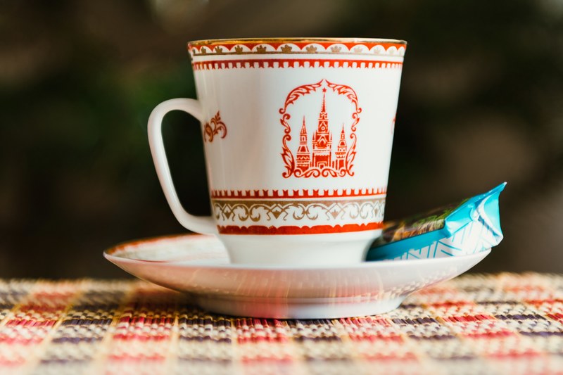 a ceramic cup with a castle on it sitting on a saucer with a biscuit in a wrapper, kremlin cup of tea with candy_ 4k