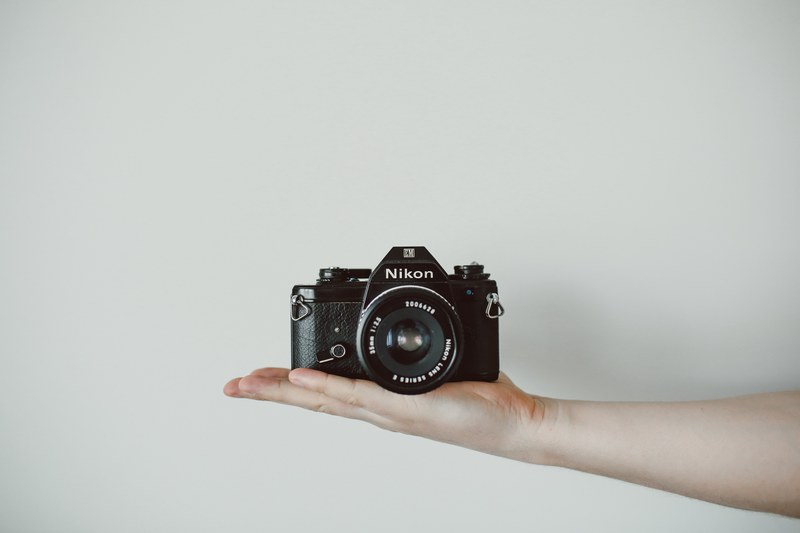 a person holding a nikon camera in the palm of their hand against a white wall, nikon film camera 4k