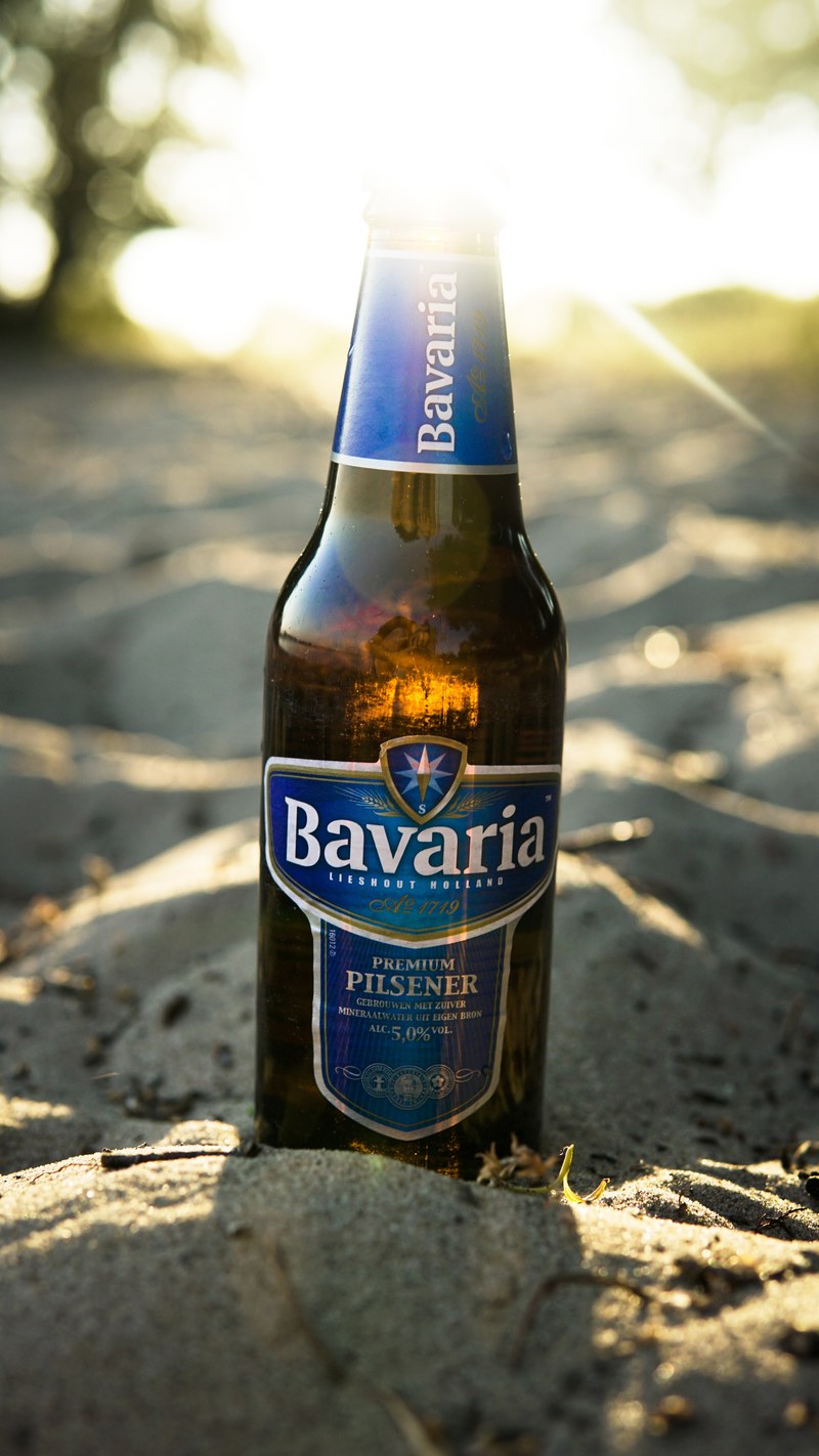 a macro view of a bavarian beer bottle on the sand in summer netherlands, a beer on sand 4k