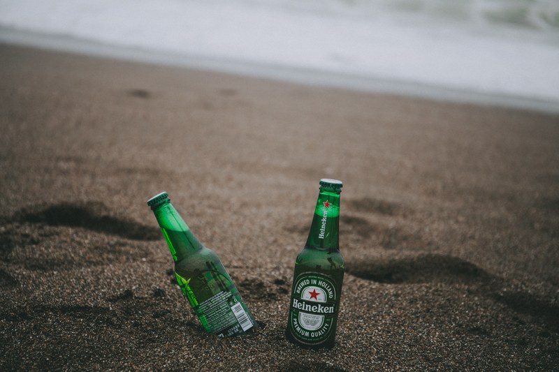 two heineken bottles beside each other one tilted placed on a sandy point reyes beach, beer by the beach 4k