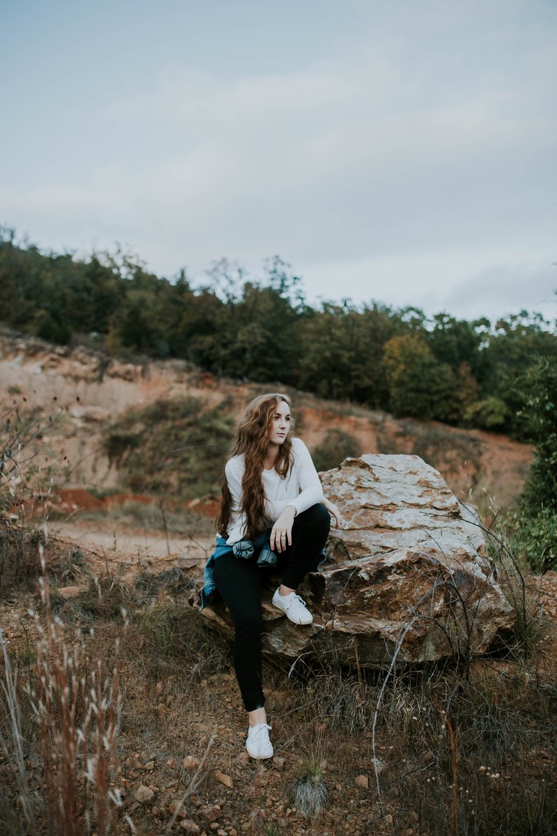 young woman sitting on a large rock during a mountain hike, relaxing on a rock 4k