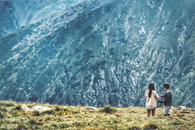 two children standing in grass with a view on a shrub covered mountain slope, romania in the eyes of a child 4k