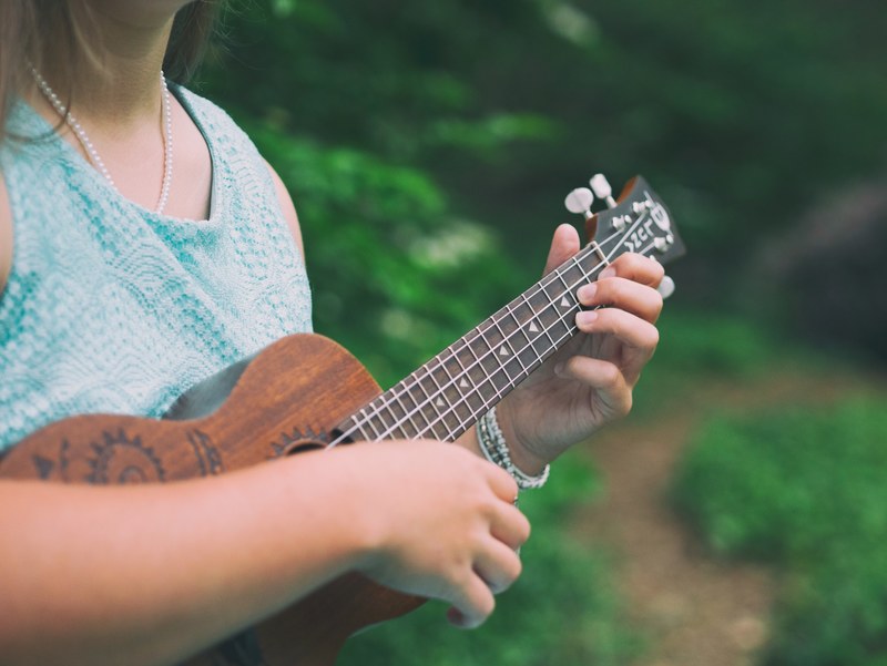 a woman in a blue dress and white pearl necklace playing ukulele, woman playing ukulele 4k