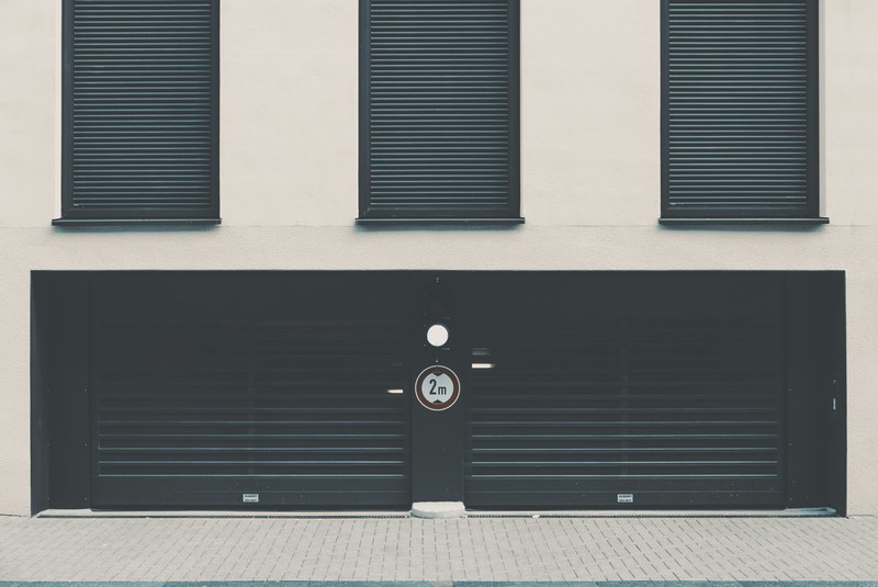 wide black metal garage door with 2m circular sign with dark window shutters above, window shutters and garage 4k