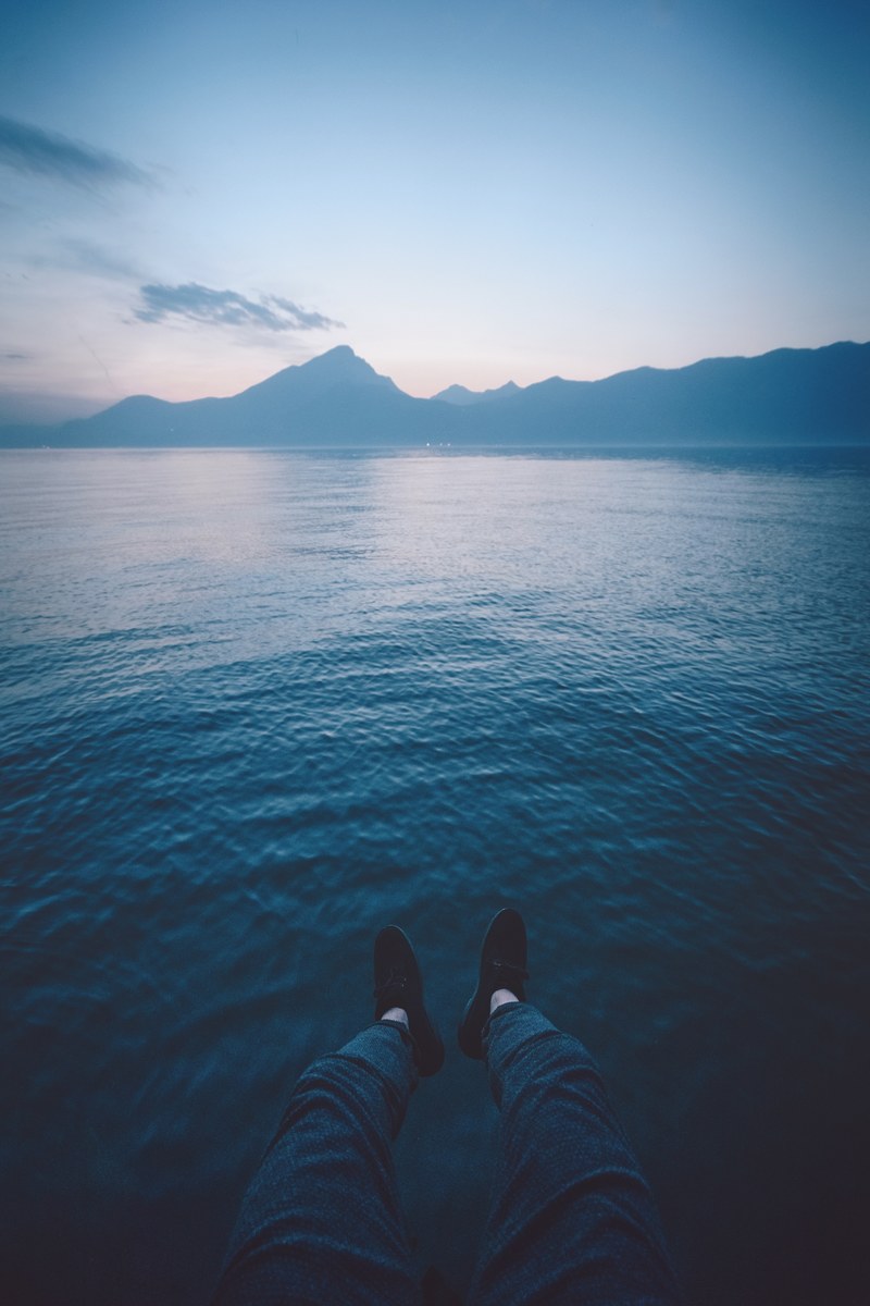 a persons feet hanging over water while overlooking the mountains in pai at sunset, blue mood 4k