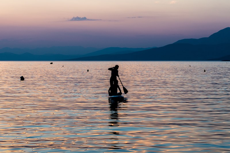 person silhouette standing on a paddle board and paddling after sunset at cariocas beach bar, person standing and paddling 4k