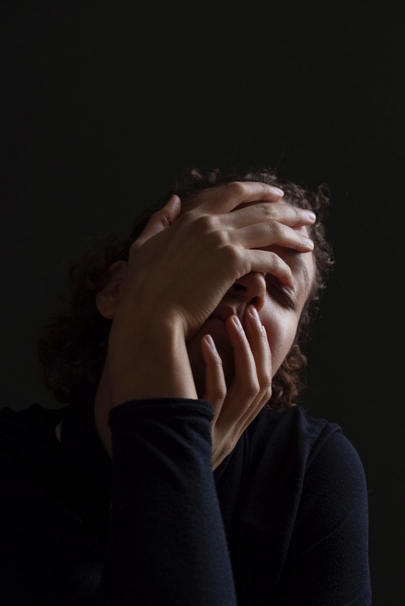 a woman in black against a black background holds both hands over her face, holding hands on face 4k