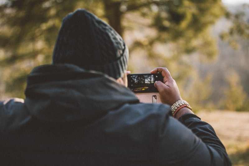 photographer in winter clothes takes a picture of trees on their smartphone, taking fall photos 4k