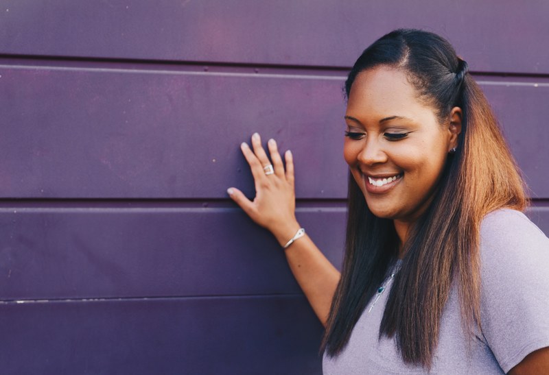 a woman with long dark hair looks downward smiling and touching a purple wall, woman touching purple wall 4k