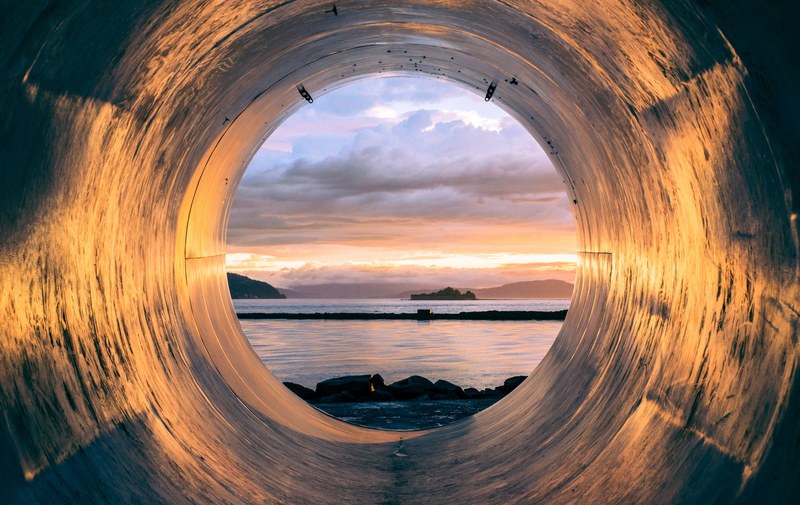 sunset over the sea seen from the inside of a large pipe, pipe by the sea 4k