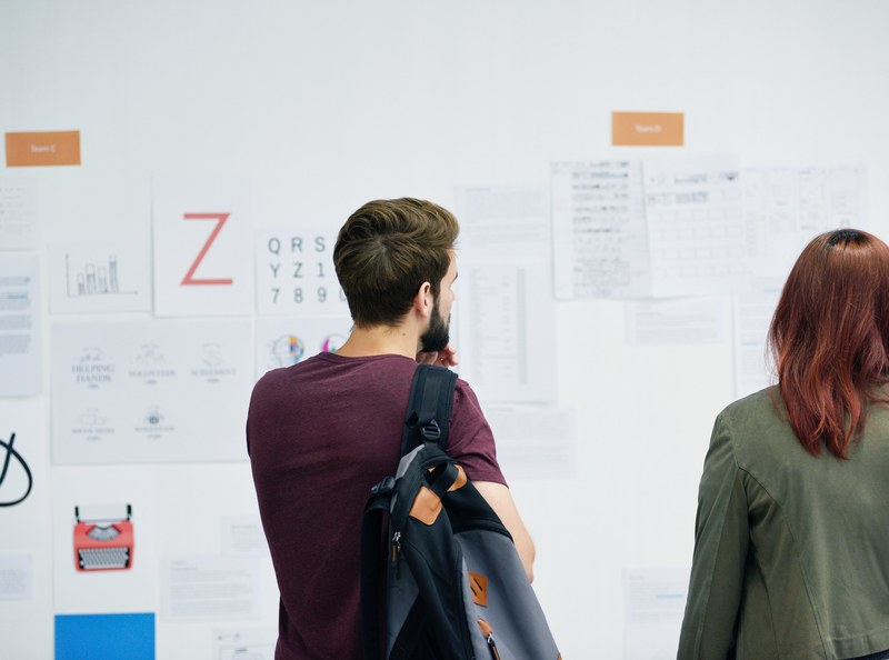 a man and a woman looking at posters on a white wall, prints on a wall 4k
