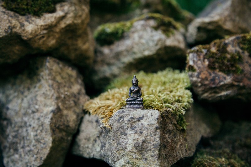 small stone buddha statue on a mossy rock surrounded by other large rocks, serene buddha statue outside 4k