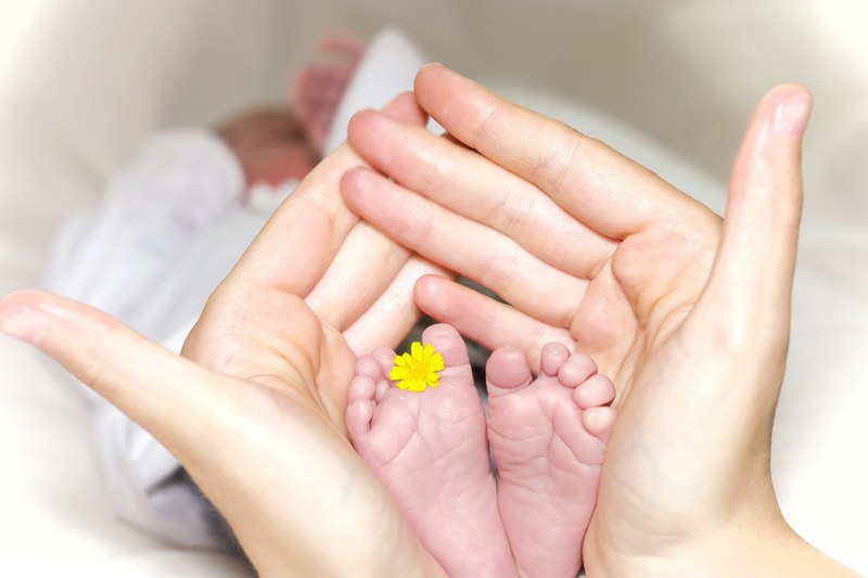 a person holding a babys feet with a yellow flower between two toes, _newborn child 4k