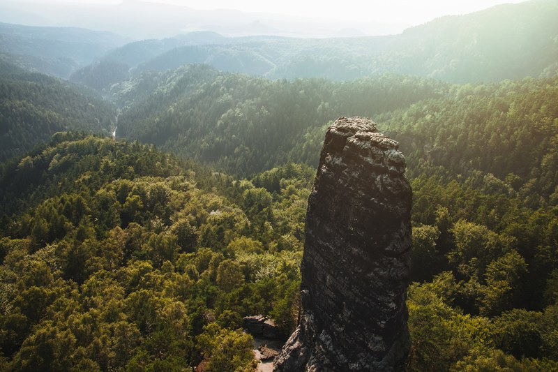 sun shines over a lush forest landscape with a tall rock formation, hensko 4k